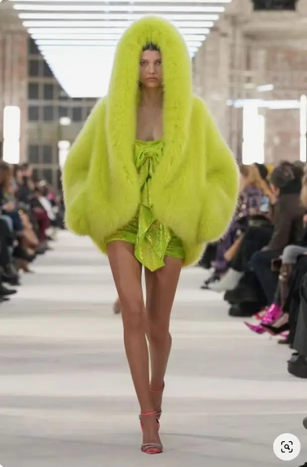 Model wearing a bright green outfit with a hood on a runway.