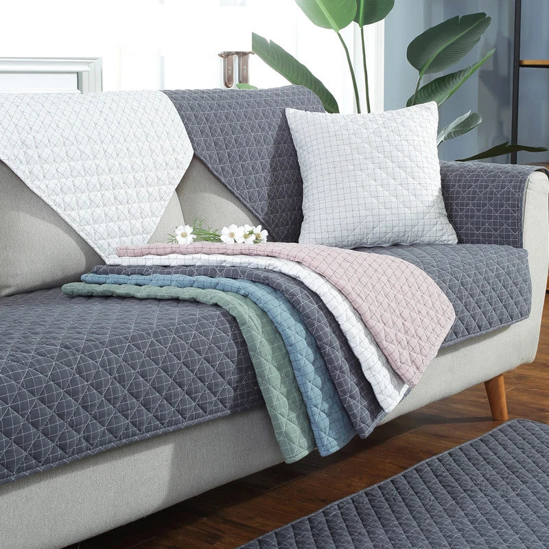 Gray quilted sofa cover on a sofa with decorative pillows and blankets.