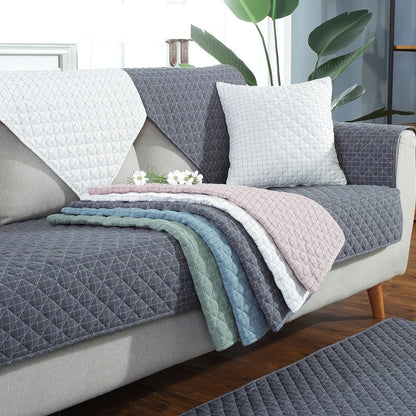 Gray quilted sofa cover on a sofa with decorative pillows and blankets.