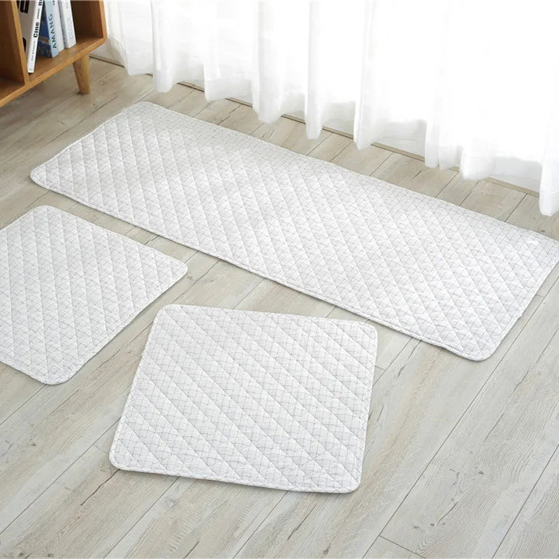 Set of three white quilted mats on a wooden floor with a bookshelf in the background.