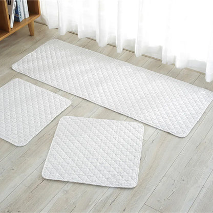 Set of three white quilted mats on a wooden floor with a bookshelf in the background.