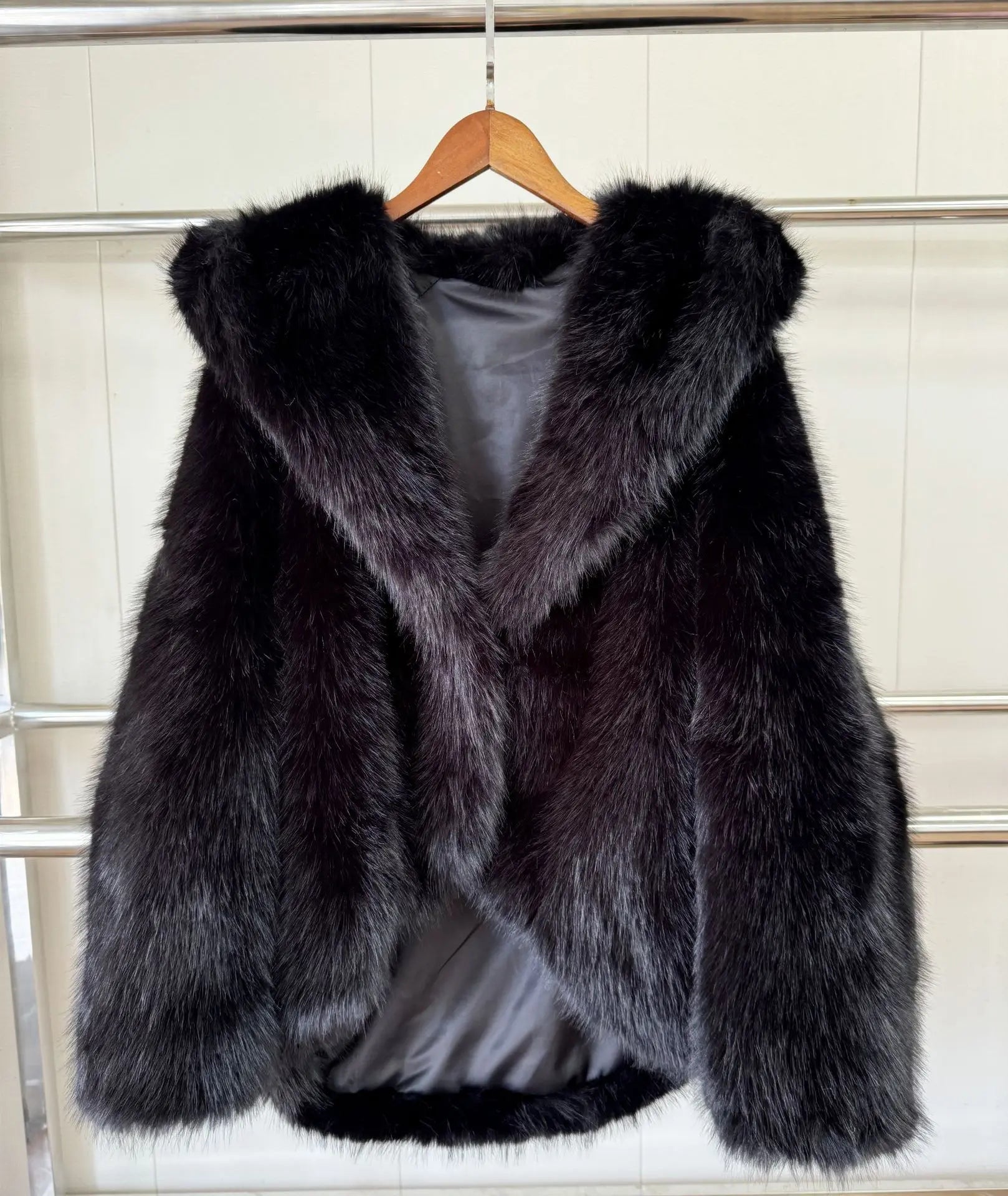 Black fur coat on a hanger against a white tiled wall.