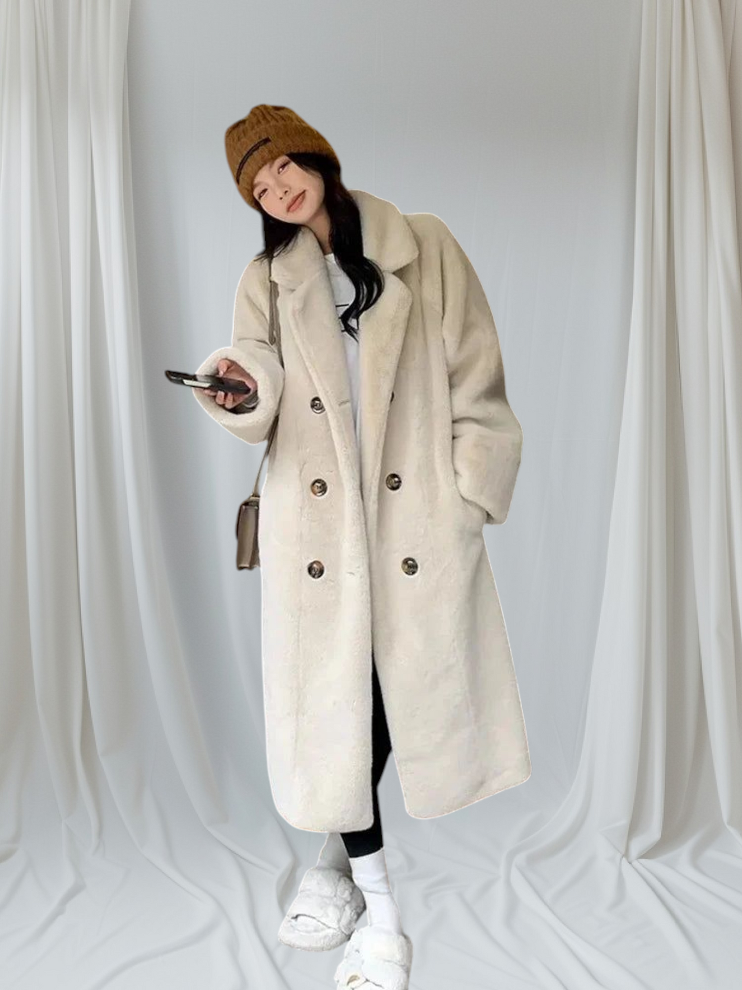 Person wearing a long beige coat, white sneakers, and a brown beanie against a plain background